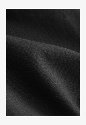 Čierna tkanina s hladkou textúrou, zobrazujúca jemné tkaniny a jemné odlesky svetla, zložená tak, aby odhalila vrstvy a hĺbku.