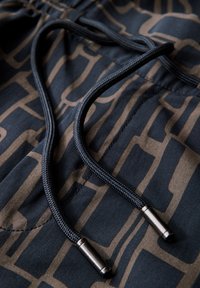 Primo piano di un tessuto con pattern, caratterizzato da linee nere e dorate, con lacci scuri e punte metalliche, che mette in risalto i dettagli di un paio di pantaloni corti.