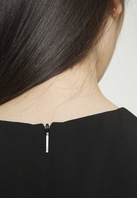 Svart plagg med en slank design, med en synlig dragkedja bak och en mjuk textur, som framhäver rena linjer och minimalistisk stil.