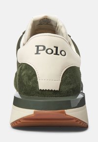 Zapatilla de hombre con parte superior de ante verde, talón de cuero crema y logotipo negro. Presenta una suela acolchada con una sección translúcida y suela de goma.