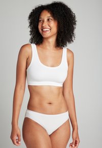 Brassiere de algodón blanco con tirantes anchos y escote redondeado, acompañado de braguitas de algodón blanco con una textura suave y un diseño minimalista.