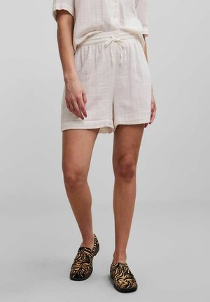 Letvægts, kremfarvede linnedshorts med elastisk talje og snøre. Sammen med sorte og brune mønstrede slip-on sko.
