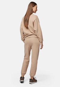 Beżowy zestaw bluz z dresami, wykonany z miękkiego materiału, z prążkowanymi mankietami i luźnym krojem, zestawiony z ciemnymi butami sportowymi.