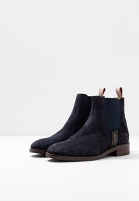 Marineblauwe suède enkelboots met elastische zijkanten en trekflappen, rechthoekige neusvorm en een houten middenzool. Minimalistisch ontwerp, veelzijdige stijl.