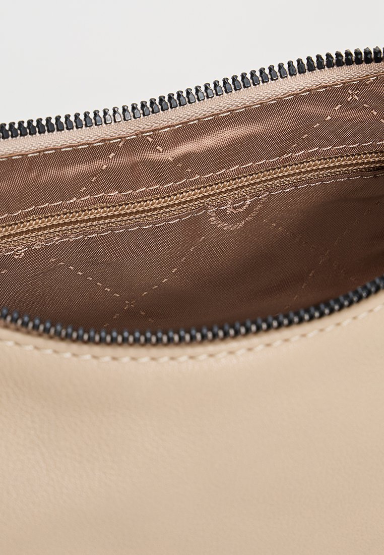 Intérieur d'un sac en cuir beige avec doublure marron matelassée, présentant une poche zippée le long du bord supérieur et un zip noir contrastant.