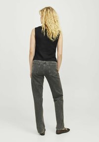 Crna majica bez rukava u kombinaciji s tamnosivim trapericama visokog struka. Odijelo se odlikuje minimalističkim dizajnom i ravnim krojem.