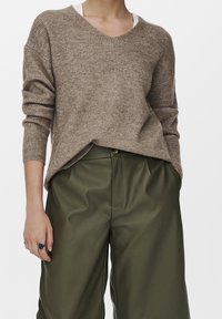 Pull en maille côtelée marron avec col en V et épaules tombantes, associé à un pantalon taille haute vert olive. Comprend des poches latérales.