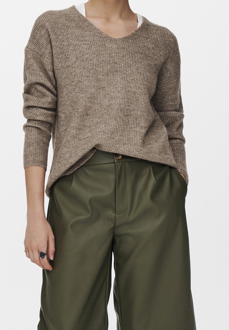 Pull en maille côtelée marron avec col en V et épaules tombantes, associé à un pantalon taille haute vert olive. Comprend des poches latérales.