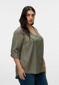 Chemise olive verte à col en V, manches trois-quarts retroussées avec un onglet, en tissu texturé et à coupe ample.