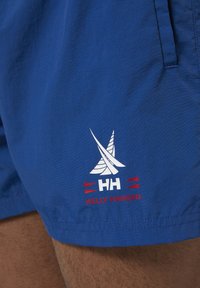 Pantalones cortos azules de tela ligera con un logotipo de vela blanca y acentos rojos. Incluye el texto "HH" y "HELLY HANSEN" en la parte frontal.