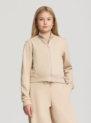 Giacca beige con zip frontale, colletto alto e polsini a coste, realizzata in tessuto morbido, abbinata a pantaloni beige coordinati. Design semplice e lineare.