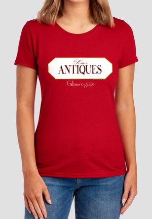 Woman wearing a red T-shirt with a white sign reading "Kim's Antiques" and "Gilmore girls" in small text below.
