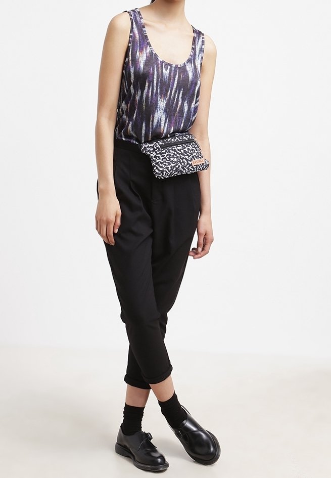 Top sans manches violet et noir à motifs avec un décolleté en forme de scoop, associé à un pantalon noir ajusté et un sac banane à motifs noir et blanc.
