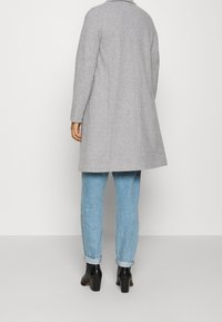 Grijze wollen jas met een rechte snit, lange mouwen en een kraag, gecombineerd met lichtblauwe spijkerbroek en zwarte enkellaarsjes.