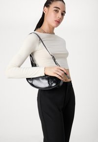 Sac à main en cuir noir avec une forme arrondie, doté de clous argentés, d'une fermeture éclaire et d'un détail de bandoulière tressée.