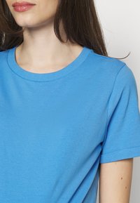 Niebieska, krótka koszulka z miękkiej bawełny. Posiada okrągły dekolt i gładką teksturę bez widocznych wzorów czy akcentów.