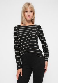 Camisola preta de mangas longas com riscas horizontais em creme, apresentando um decote barco e um corte descontraído, combinada com calças pretas caneladas.