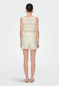 Kanten bodysuit in een crèmekleur, met een doorzichtige achterkant en een gestructureerd patroon. Vergezeld van bijpassende shorts en platte sandaal.