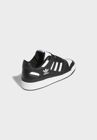Black and white sneaker with leather upper, three white stripes, padded collar, and rubber sole. Features Adidas logo on the side.
