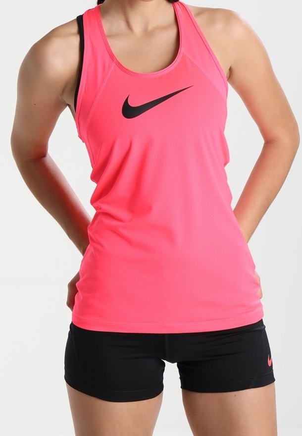 Personne en forme portant un débardeur Nike rose vif et un short de sport noir, les mains reposant sur le bas du dos.