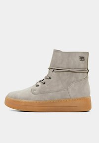 Bottes cheville en daim gris avec un bout rond, un laçage à l'avant et une semelle en caoutchouc. Elles présentent un accent cousu et un logo sur le côté.