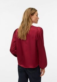 Burgunderfarget satengbluse med puffede ermer og rund hals. Glatt tekstur og løs passform. Bakfra vises en buet kant.