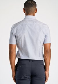Camicia a maniche corte con colletto di colore azzurro chiaro con strisce verticali bianche; abbinata a pantaloni scuri aderenti con dettagli sulle tasche posteriori.
