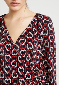 Il vestito presenta uno sfondo blu navy con una fantasia a cuori ripetuta in rosso e bianco. Il tessuto ha un aspetto testurizzato e rigato.