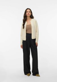 Cardigan tricoté crémeux avec un col rond, des boutons ressemblant à des perles et une texture douce, associé à un haut beige et à un pantalon noir large.