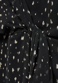 Abito in tessuto nero con motivo a macchie bianche, caratterizzato da una sezione arricciata e un dettaglio annodato. Il materiale ha una consistenza morbida con un leggero lucido.