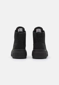 Bottines noires en daim, dotées d'une semelle en caoutchouc épaisse, d'un col rembourré et d'un branding minimal à l'arrière.