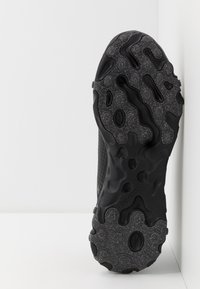 Svart sportskosula med texturerade, böljande mönster, som kombinerar släta och något fläckiga material.