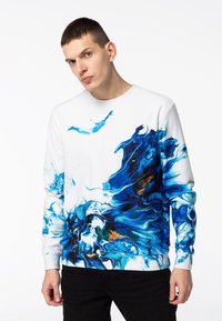Sudadera de manga larga con cuello redondo en blanco, con un patrón abstracto azul con espirales y salpicaduras. Fabricada con un tejido suave y texturizado.