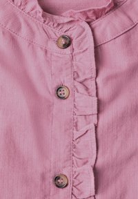 Gros plan sur un tissu en velours côtelé rose avec trois boutons marron et une bordure froncée le long de la ligne de boutons.