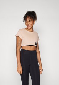 Lyserosa kortermet t-skjorte med svart "NEI"-design foran, kombinert med høyhårede svarte leggings.