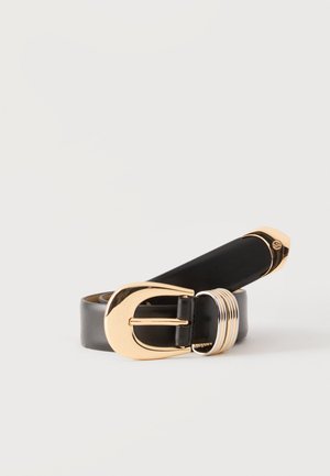 Ceinture en cuir noir roulée avec une boucle ovale dorée et plusieurs anneaux métalliques dorés sur un fond clair uni.