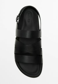 Black sandal made of leather with a flat sole. Features crossed straps and an open back. Smooth texture with a minimalist design.