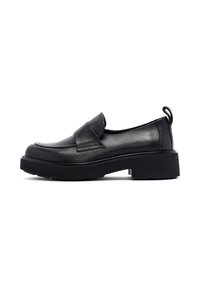 Mocasines de cuero negro con punta redondeada, tacón bajo y decorativa solapa. Presentan una lengüeta en la parte posterior y suela texturizada.