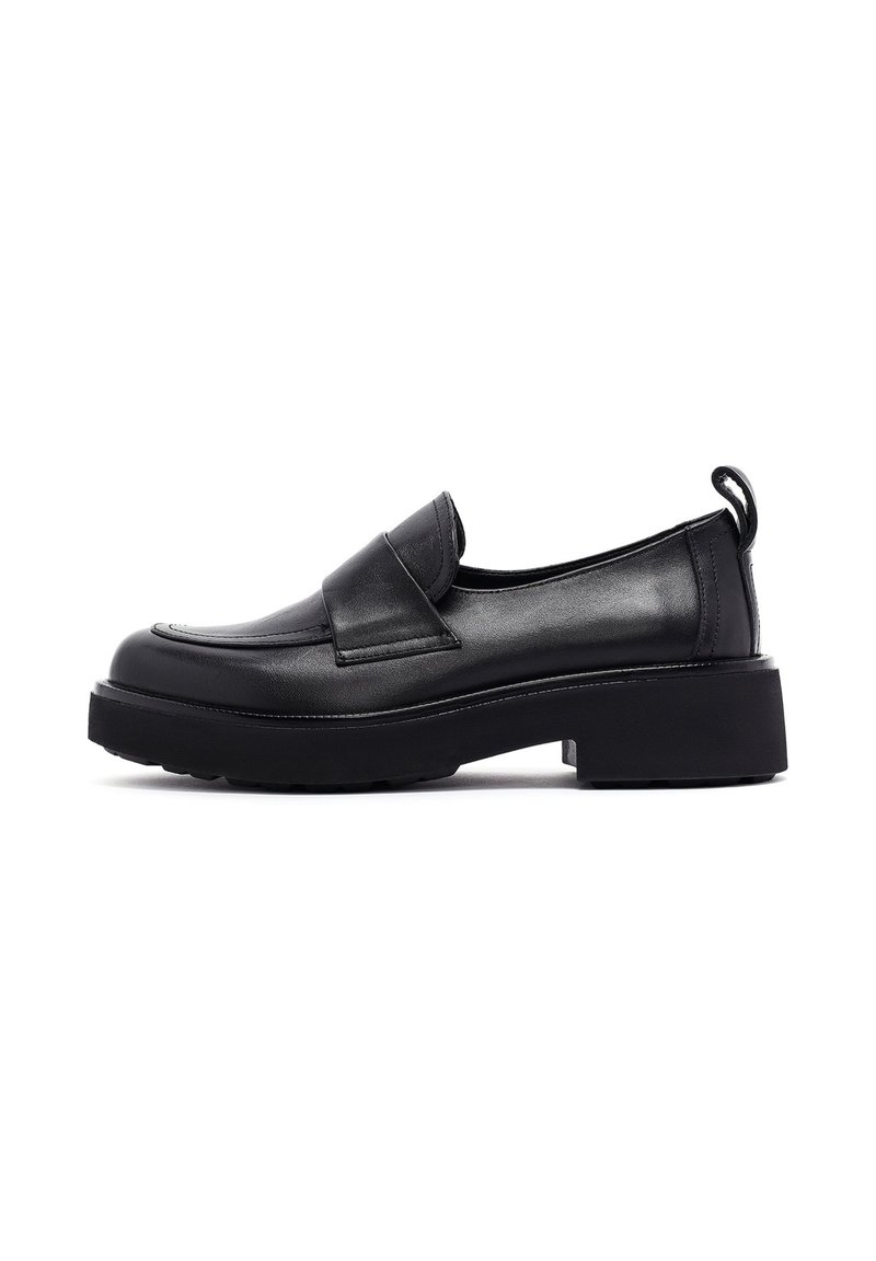 Mocasines de cuero negro con punta redondeada, tacón bajo y decorativa solapa. Presentan una lengüeta en la parte posterior y suela texturizada.
