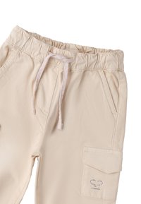 Beżowe dresy z bawełny z elastycznym paskiem, sznurkiem do ściągania, bocznymi kieszeniami i naszywaną kieszenią z srebrnymi akcentami. Gładka tekstura.