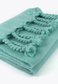 Une couverture tricotée vert menthe présentant un design texturé avec des accents tressés et des pompons moelleux le long des bords, fabriquée en laine douce.