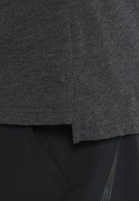 Camisa gris de manga corta con una textura suave, que presenta una abertura lateral en el dobladillo, combinada con pantalones deportivos negros con bolsillos discretos.
