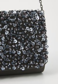 Borsa in tessuto nero adornata con gruppi di paillettes e perline, caratterizzata da una superficie testurizzata e una corta tracolla in metallo.
