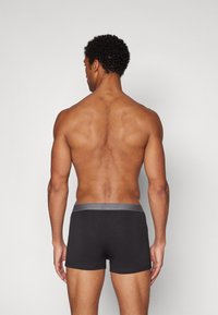 Schwarze Boxershorts mit einem grauen Bund, aus einem glatten Stoff gefertigt. Das Modell wird von hinten gezeigt, um die Passform und das Design zu präsentieren.