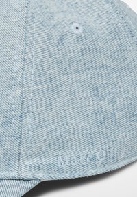 Hellblaue Denim-Kappe mit gestickten Nähten, gebogenem Schirm und dezentem Branding am Rand. Verfügt über ein Belüftungsloch an der Spitze.