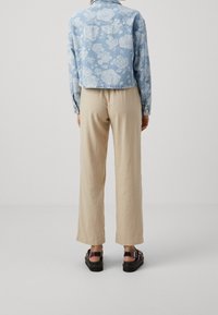 Chaqueta de mezclilla azul claro con estampado floral blanco, combinada con pantalones de pierna ancha beige y sandalias negras con suela gruesa.