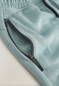 Hellblaue Sweatpants zeichnen sich durch einen strukturierten Stoff, einen elastischen Bund und eine mit schwarzem Beschlag versehenen Reißverschlusstasche für sicheren Stauraum aus.