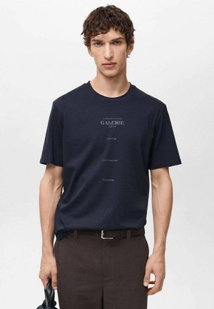 Tricou din bumbac bleumarin, cu mâneci scurte și guler rotund, având inscripția „GALERIE 1974” și alte expresii imprimate cu cerneală mai deschisă pe față.