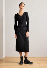 Top negro de manga larga con canalé y cierre, combinado con una falda negra fluida y calzado negro de tobillo con suela. Textura suave.