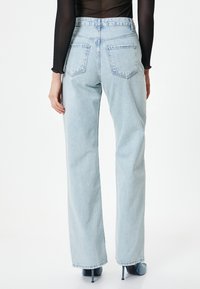 Jeans de tiro alto azul claro con un corte relajado, dos bolsillos traseros y un diseño de pierna recta, combinados con tacones de aguja azules.